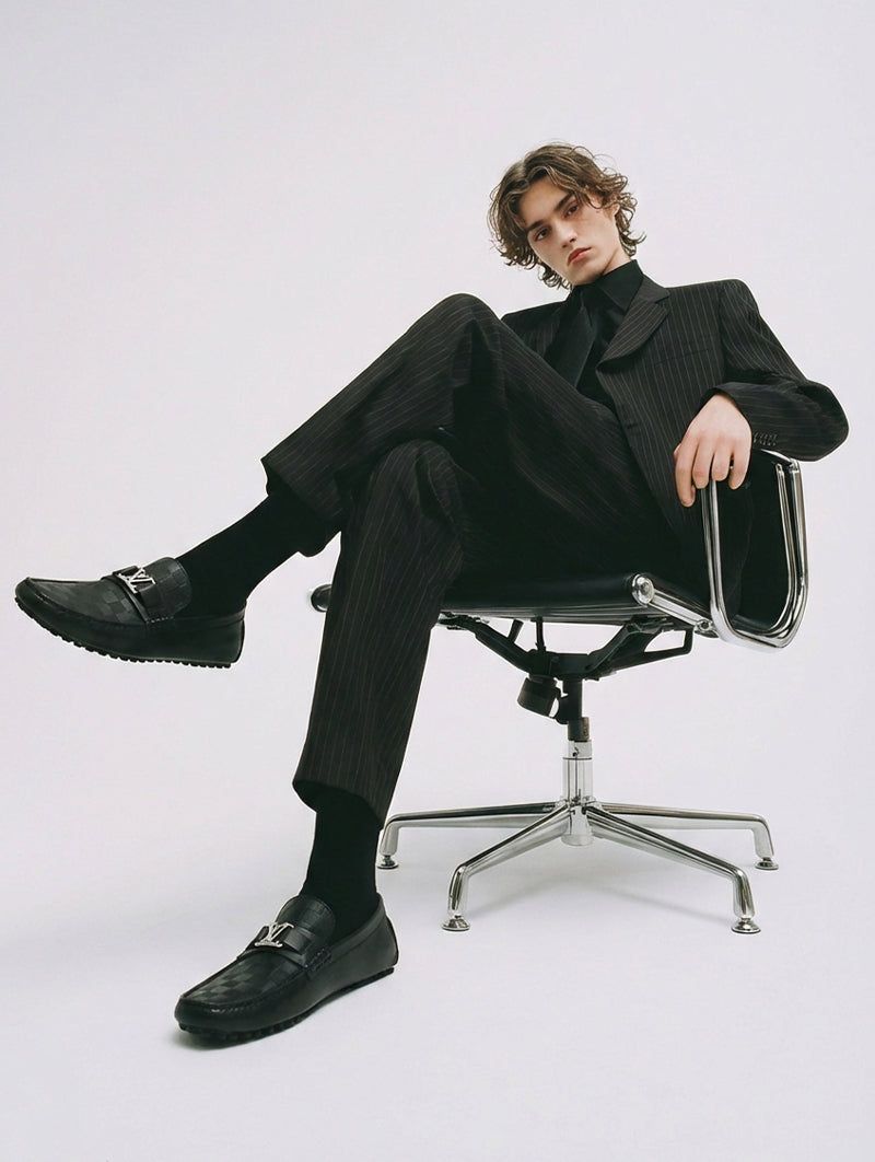 Man in a black suit and loafers seated on an office chair